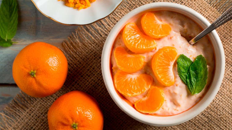 Schale mit Joghurt, Mandarinenstücken und Minzblättern, daneben zwei ganze Mandarinen und ein Teller mit geriebener Orangenschale.