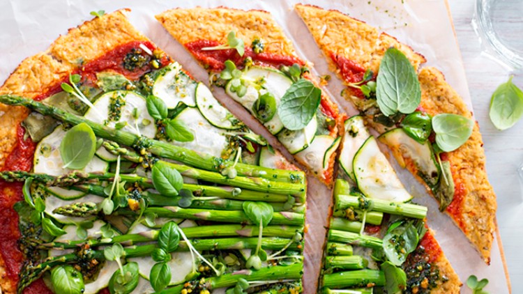 Knusprige Pizza mit rotem Tomatenbelag, grünem Spargel, Zucchinischeiben, Kräutern und frischen Basilikumblättern.