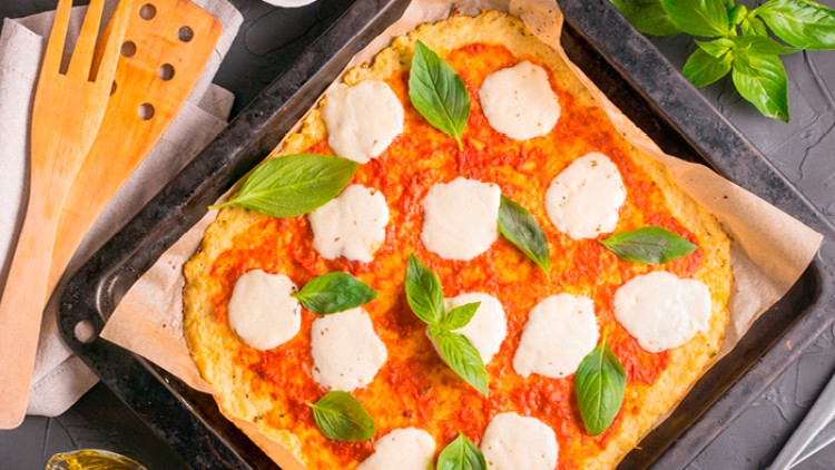 Rechteckige Pizza mit Tomatensauce, Mozzarella und frischen Basilikumblättern auf Backpapier auf einem Backblech.