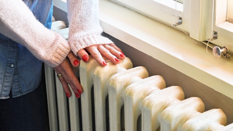Hände mit rotem Nagellack liegen auf einem weißen Heizkörper unter einem Fenster mit Vorhangschnur.