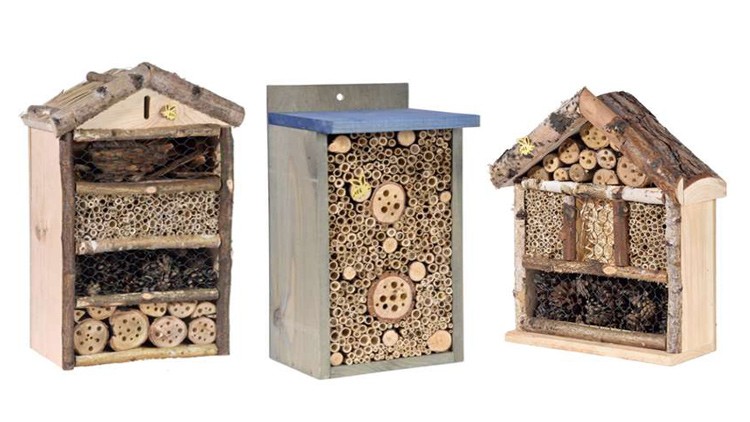Drei verschiedene, aus Holz gefertigte Insektenhotels mit Naturmaterialien wie Bambus, Tannenzapfen und Ästen.