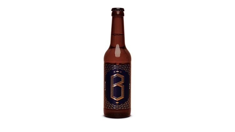 Braune Glasflasche mit dunkelblauem Etikett, darauf ein großes goldfarbenes „B“ und geometrische Muster.