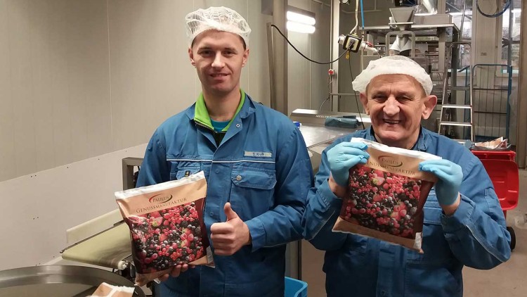 Zwei Personen in blauer Arbeitskleidung und Haarnetzen halten Packungen mit gemischten Beeren in einer Produktionshalle.