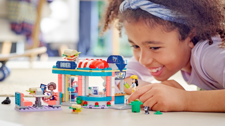 Ein buntes Spielzeug-Diner aus Bausteinen mit Figuren und Zubehör steht auf einem Tisch in einem hellen Raum.