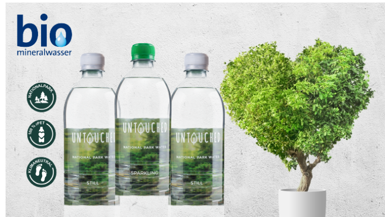 Drei Mineralwasserflaschen mit Aufschrift „UNTOUCHED National Park Water“ neben Bio-Logo und grünem Herzbaum in weißem Topf.