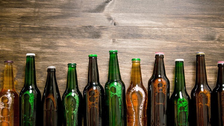 Verschiedene leere Bierflaschen in Grün und Braun stehen in einer Reihe vor einer Holzwand.