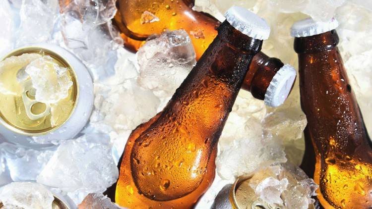 Braune Glasflaschen und goldene Getränkedosen liegen zwischen Eiswürfeln, Flaschen mit Kronkorken verschlossen.