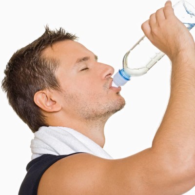 Person mit weißem Handtuch um den Nacken trinkt Wasser aus einer transparenten Flasche.