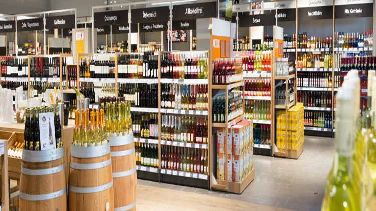 Ein GLOBUS-Getränkebereich mit Regalen voller Flaschen, darunter Wein, Secco und alkoholfreie Getränke, sowie Holzweinfässer im Vordergrund.