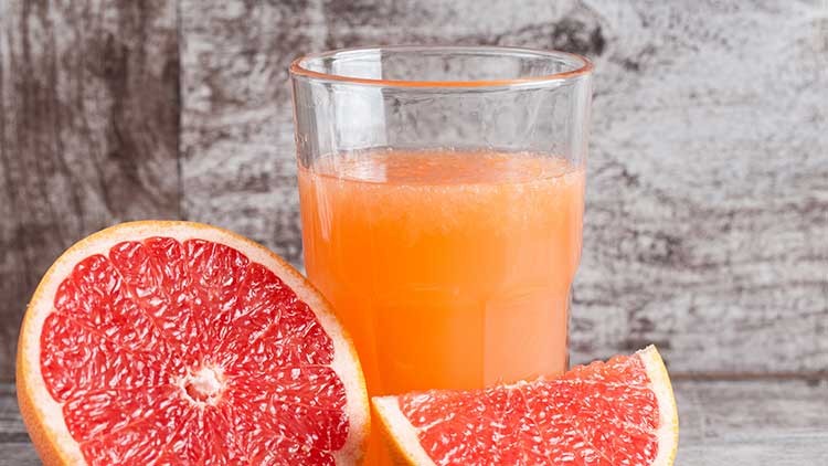 Ein gefülltes Glas mit orangefarbenem Grapefruitsaft steht neben einer halben und einer geviertelten Grapefruit.