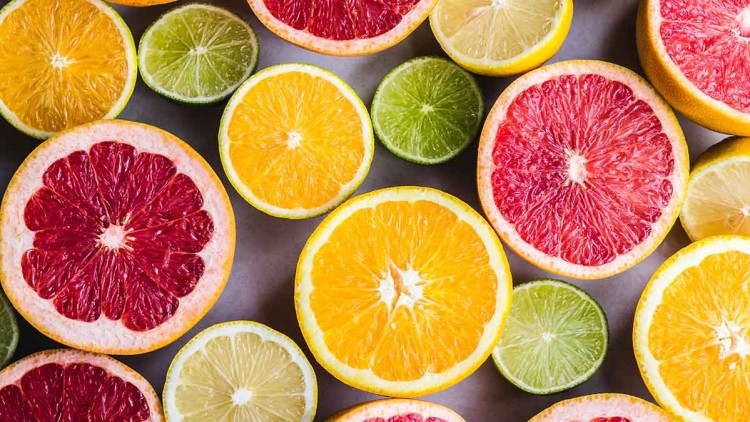 Halbierte Zitrusfrüchte in verschiedenen Farben wie Gelb, Orange, Rot und Grün liegen bunt gemischt auf einer grauen Fläche.