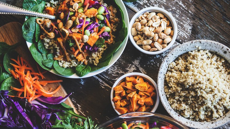 Schale mit Blattspinat, Quinoa, Süßkartoffeln, Erdnüssen, Rotkohl, Karotten und Dressing, daneben Beilagen in Schalen.