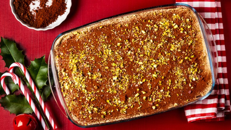 Ein rechteckiges Dessert mit Kakao und gehackten Pistazien in einer Glasform, daneben Zuckerstangen und ein rotes Tuch.