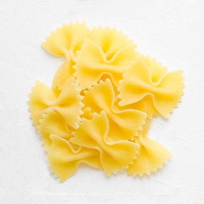 Mehrere ungekochte Farfalle-Nudeln in Gelb liegen auf einer weißen Oberfläche.