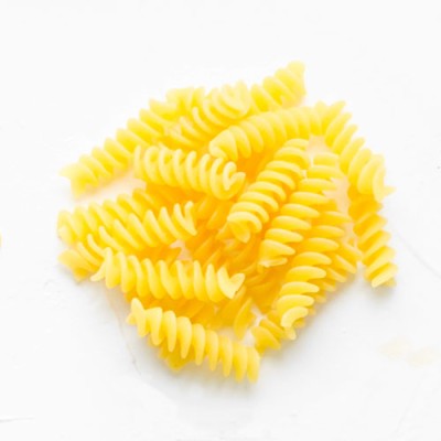 Gekochte Gelb-Weizen-Fusilli-Nudeln liegen auf einer weißen, leicht feuchten Oberfläche.