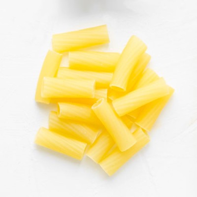 Gelbe, ungekochte Rigatoni-Nudeln liegen verteilt auf einer weißen, glatten Oberfläche.