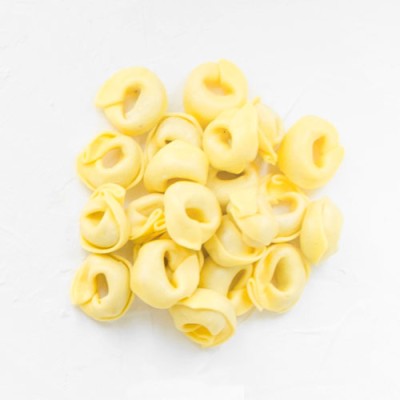 Gelbe, ungekochte Tortellini liegen auf einer weißen Oberfläche.