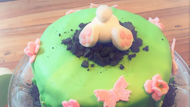 Grüne Torte mit Blumen und Schmetterlingen aus Fondant, Erdboden aus Kekskrümeln und Hasenfüßen aus Marzipan obenaufs.