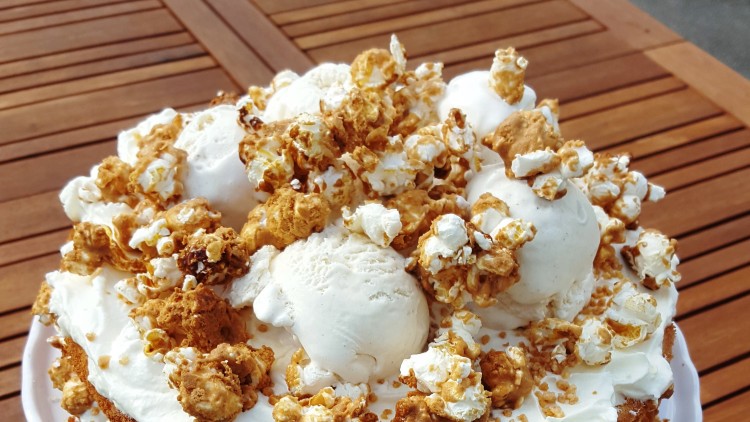 Runder Kuchen mit zwei Schichten, Sahne, Eiskugeln und karamellisiertem Popcorn auf einer weißen Tortenplatte.