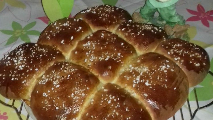 Ein goldbraunes Hefegebäck mit Zucker bestreut auf einem Gitter, daneben eine Hasenfigur und eine Blume auf einer Tischdecke.