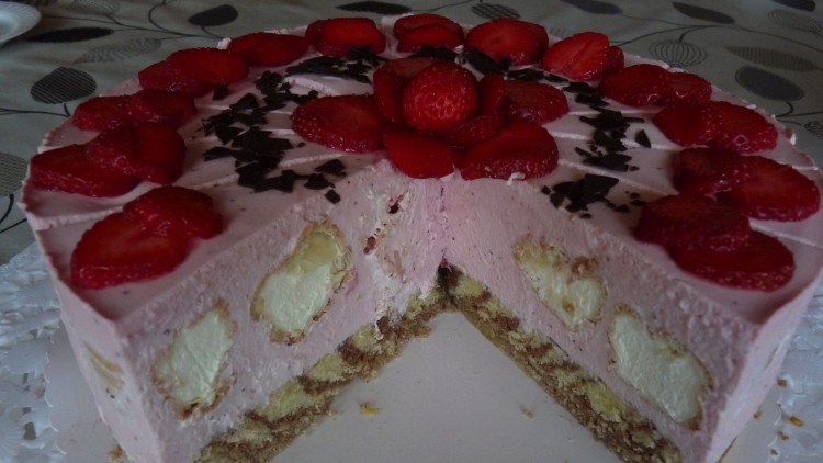 Erdbeer-Sahnetorte mit roten Erdbeerscheiben, Schokostreuseln und angeschnittenem Stück auf weißer Tortenplatte.