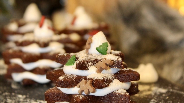 Gestapelte, sternförmige Lebkuchen mit weißer Cremefüllung und Dekoration aus kleinen Zuckerfiguren auf dunkler Unterlage.