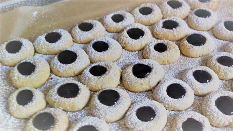 Runde Plätzchen mit Puderzucker und dunkler Marmelade in der Mitte liegen auf braunem Backpapier.