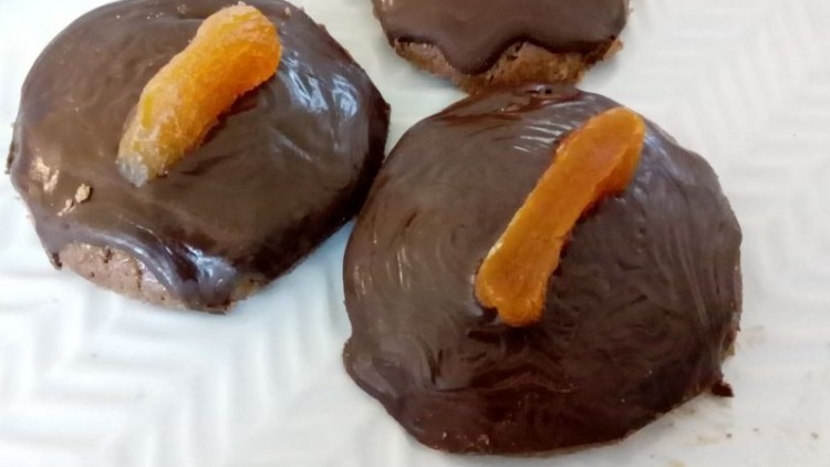 Drei mit Schokolade überzogene Kekse, jeweils mit einer getrockneten Orangenscheibe dekoriert, auf einem weißen Teller.