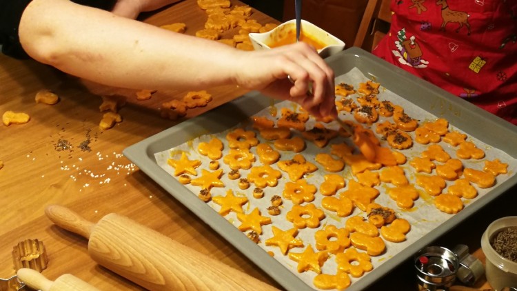 Ein Backblech mit orange glasierten Plätzchen in Stern- und Blumenform wird von Hand mit Kräutern bestreut.