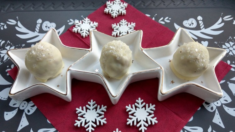 Drei weiße Pralinen mit Zuckerdekor liegen in sternförmigen Schalen auf einem roten Untergrund mit weißen Schneeflocken.