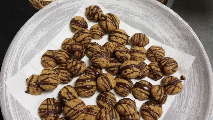 Kleine Kekse mit Schokoladenstreifen liegen auf weißen Servietten auf einem großen runden Teller, daneben Dekokugeln und eine Kerze.