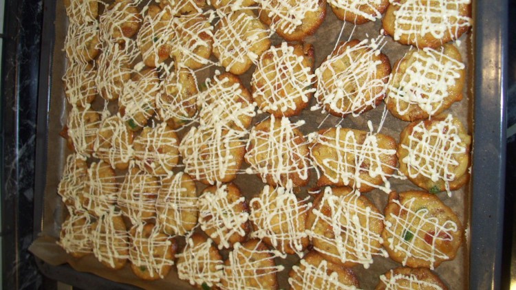 Goldbraune Plätzchen mit heller Verzierung aus Zuckerglasur liegen dicht aneinander auf einem mit Backpapier ausgelegten Backblech.