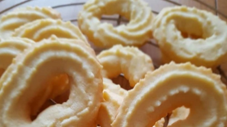 Butterplätzchen in Kringelform liegen auf einem runden Kuchengitter aus Metall auf einer Holzoberfläche.