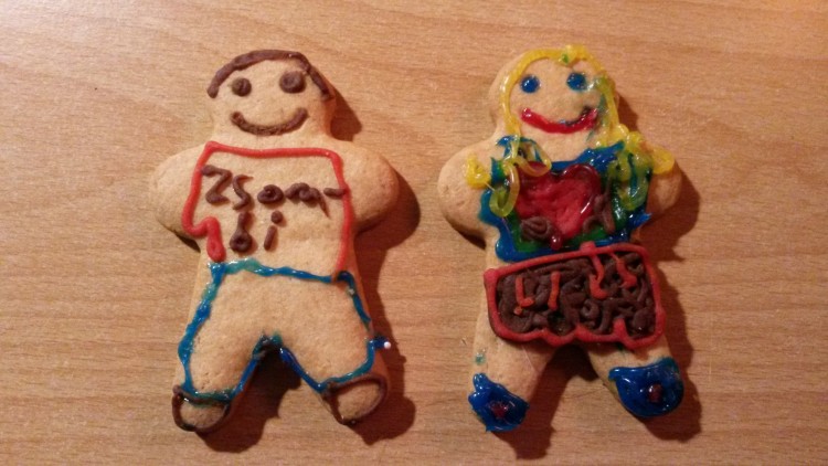Zwei Lebkuchenfiguren mit bunter Zuckerdekoration, linker Keks mit Aufschrift „Zsobi“ und rechter Keks mit rotem Herz auf Holzuntergrund.
