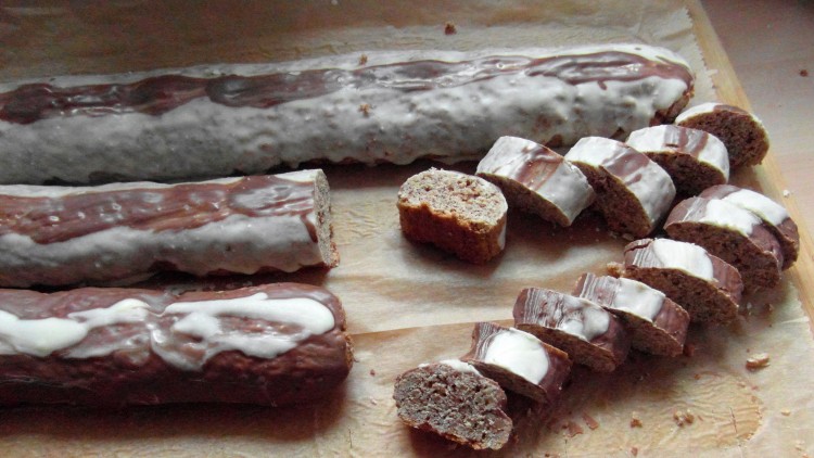 Drei lange, mit Schokolade und Zuckerguss überzogene Lebkuchenrollen, teils angeschnitten, auf braunem Backpapier.