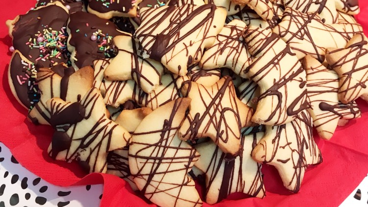 Butterplätzchen mit Schokoladenglasur und bunten Streuseln liegen auf einem roten Tuch auf einem Teller.