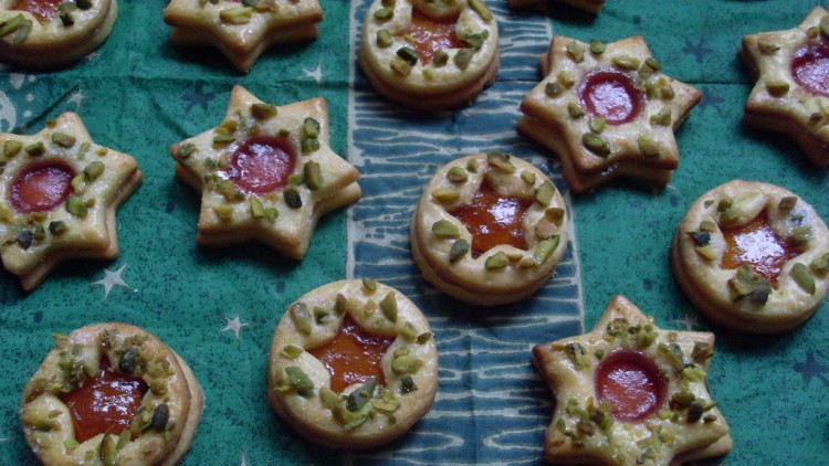 Stern- und kreisförmige Plätzchen mit roter Marmelade in der Mitte und Pistazienstückchen auf grünem Untergrund.