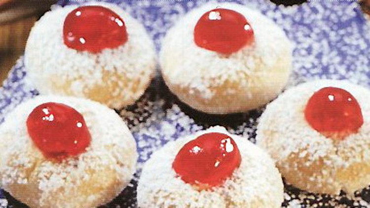 Fünf runde Gebäckstücke mit Puderzucker bestreut, jedes mit einem roten Klecks Marmelade in der Mitte, auf blauem Untergrund.