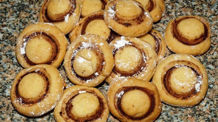Runde Kekse mit braunem Kreis-Muster und Puderzucker auf einer gemusterten Steinplatte.