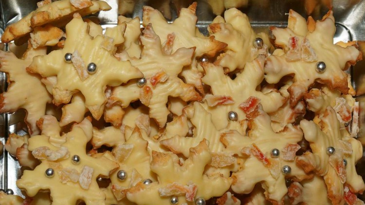 Plätzchen in Sternform mit weißer Glasur, kandierten Früchten und silbernen Zuckerkugeln auf einem Tablett.