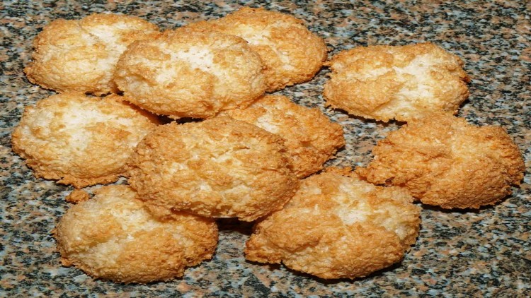 Mehrere goldbraune Kokosmakronen liegen auf einer gemusterten, grauen Granitoberfläche.