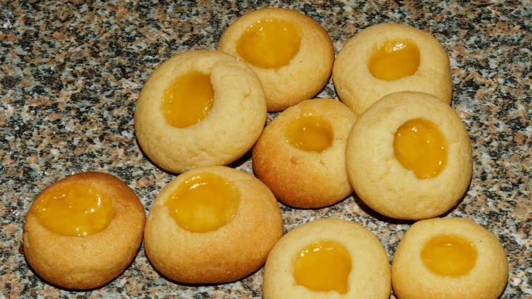 Runde Buttergebäck-Kekse mit gelber Füllung in der Mitte liegen auf einer granitartigen Oberfläche.