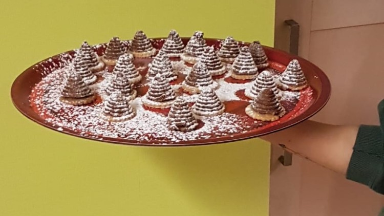 Eine Hand hält ein rotes Tablett mit vielen kleinen Tannenbaum-Gebäcken, die mit Puderzucker bestreut sind.