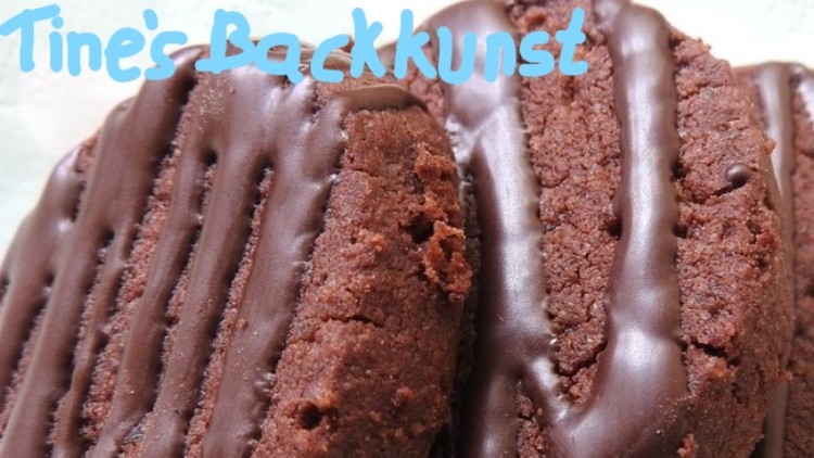 Nahaufnahme von mehreren Schokoladenkeksen mit Zartbitterschokoladenstreifen, oben steht in blauer Schrift „Tine’s Backkunst“.