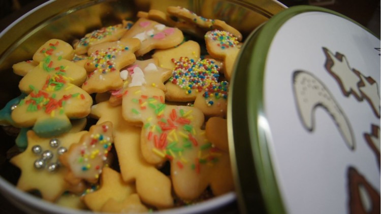 Bunte Plätzchen in verschiedenen Formen mit Zuckerguss und Streuseln liegen in einer geöffneten Blechdose mit Dekordeckel.