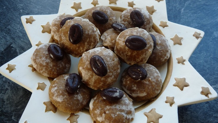 Braune Plätzchen mit Puderzucker und Schokodekoration auf einem sternförmigen Teller mit goldenen Sternen.