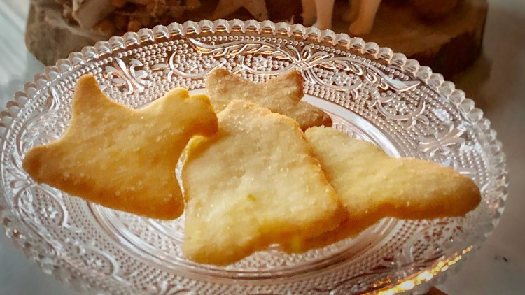 Plätzchen in Stern- und Tannenbaumform auf einem gläsernen Teller, dahinter Kerzen, Dekostern und weiße Rentierfigur.