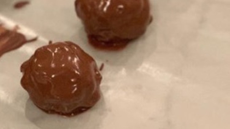 Pralinen mit glänzendem Schokoladenüberzug liegen auf einer weißen Unterlage, teilweise mit kleinen Schokoladenflecken.