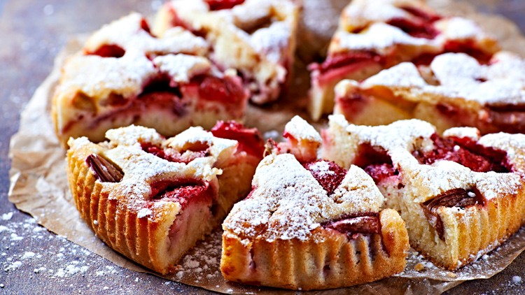 Ein runder Obstkuchen mit Erdbeeren und Puderzucker in Stücke geschnitten auf braunem Backpapier.