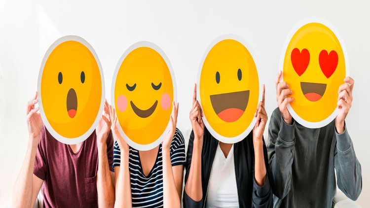 Vier Personen halten gelbe Pappschilder mit unterschiedlichen Emoji-Gesichtern wie erstaunt, glücklich, lachend und verliebt vor ihre Köpfe.